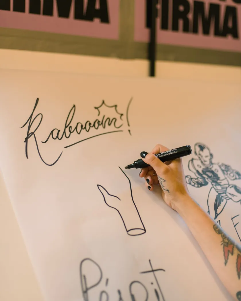Mano trazando con rotulador negro una onomatopeya y una figura sobre una hoja grande de papel blanco
