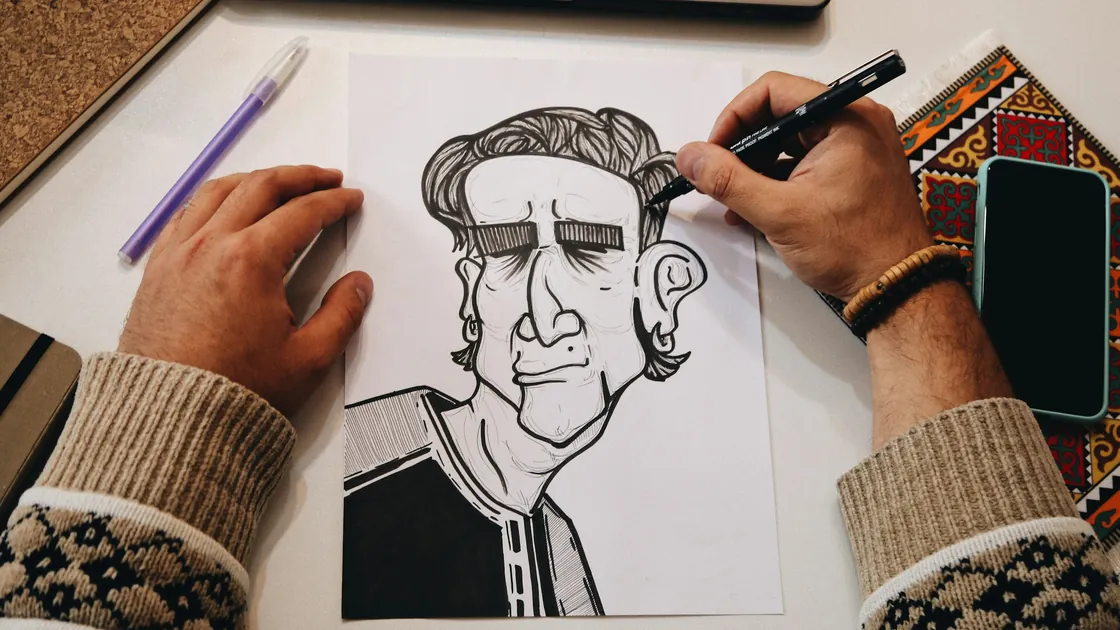 Manos entintando con rotulador negro un rostro dibujado a línea sobre papel, con el lápiz previo todavía visible
